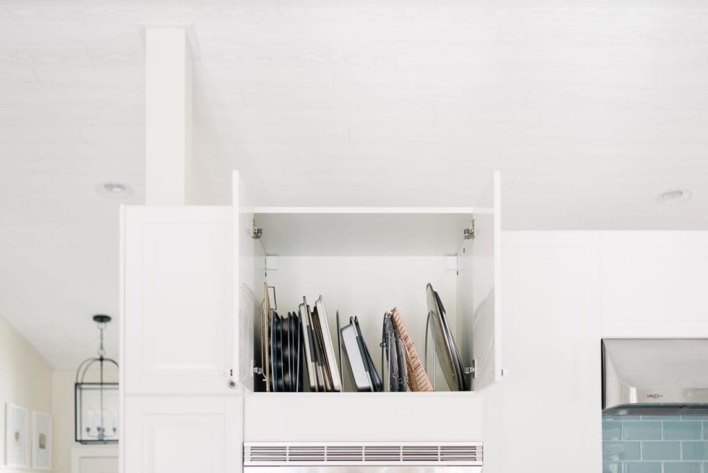 Cooling racks are stored vertically in the cupboard above the ovens to save space in a small kitchen