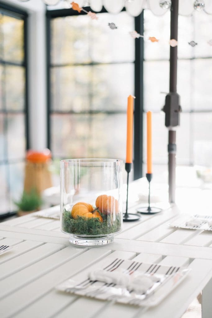 orange candles and pumpkins in glass vases sitting on moss
