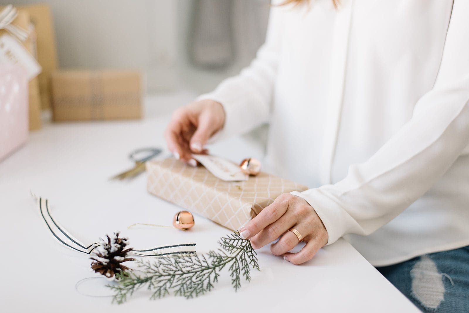 A gift being wrapped with brown paper, greenery and brass bells