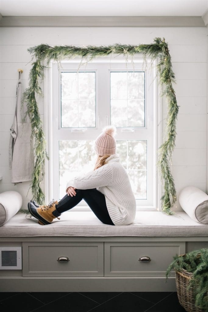 woman sitting in front of a window in winter boots and hat