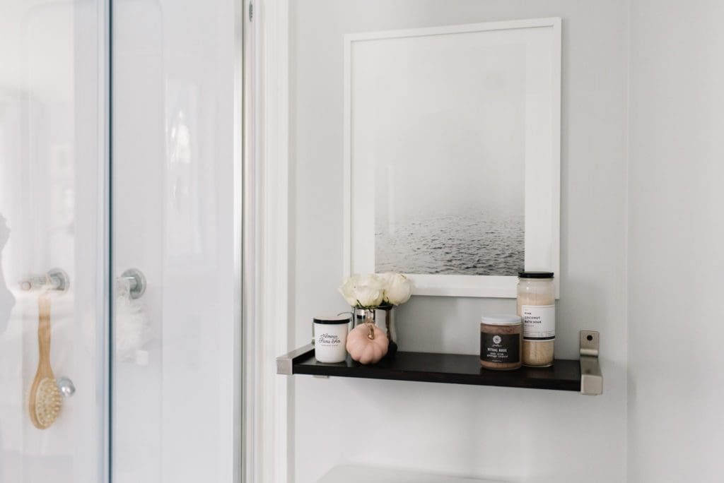 small shelf above the toilet holds accessories with art above