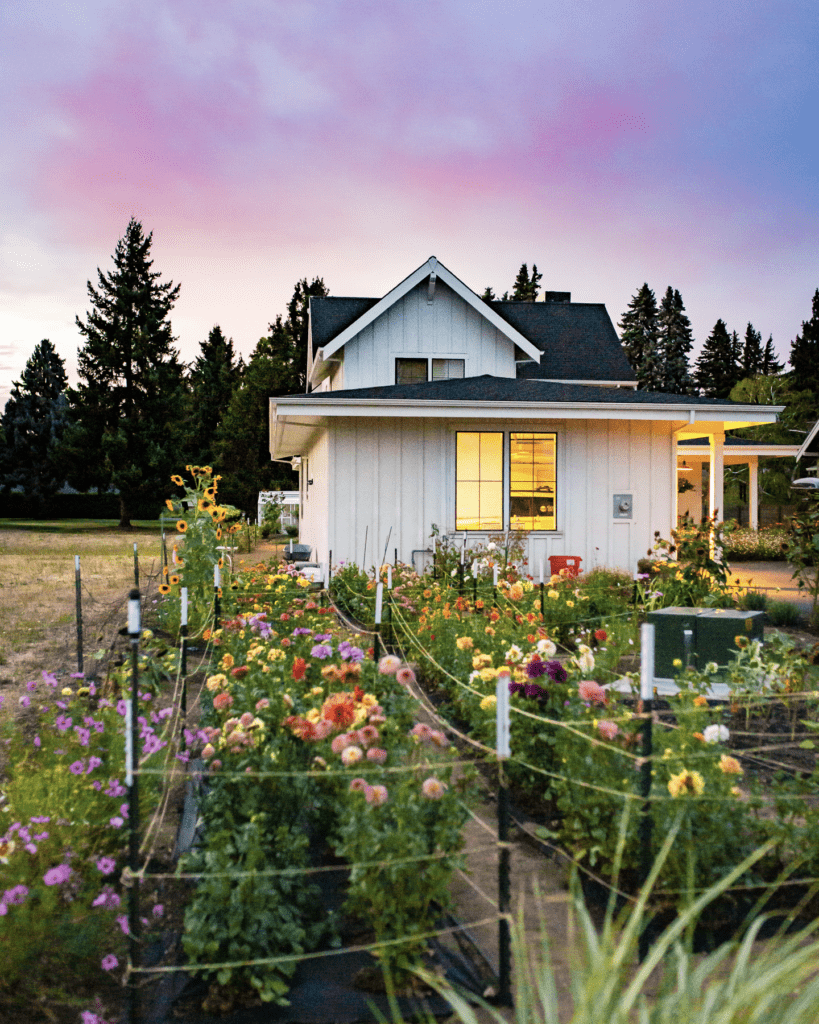 A close up of a flower garden in front of a farmhouse