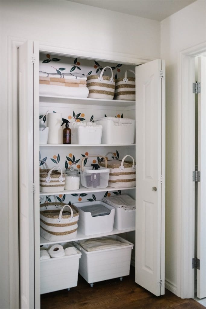 linen closet with orange pattern wallpaper and white baskets