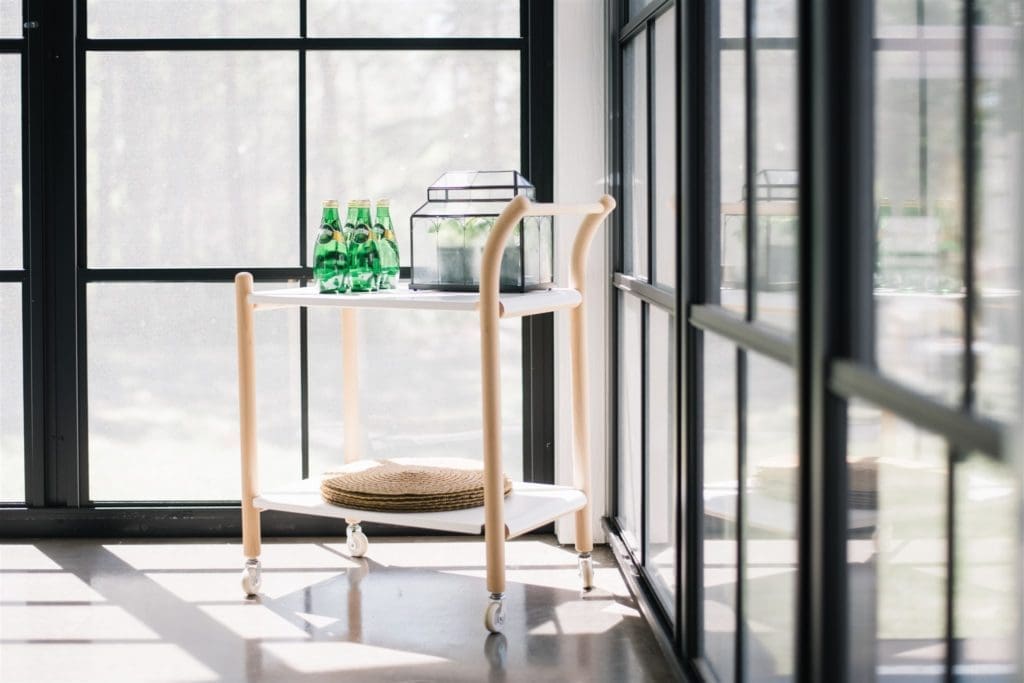 a white and wood bar cart sits in the corner of a sun room