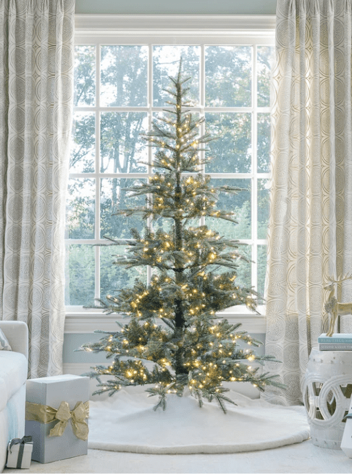 A room filled with furniture and a large window with a lit Christmas tree in front