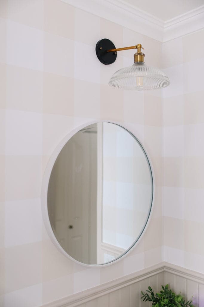 A black and brass light fixture above a round bathroom mirror