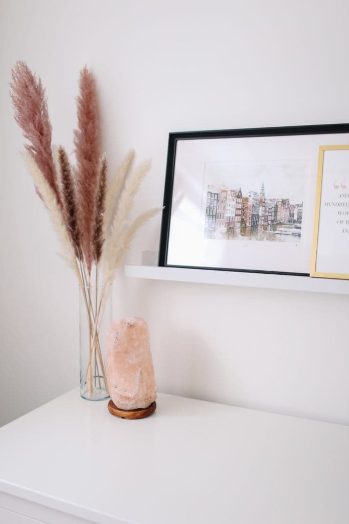 A vase of flowers on bedroom dresser with art prints on a shelf