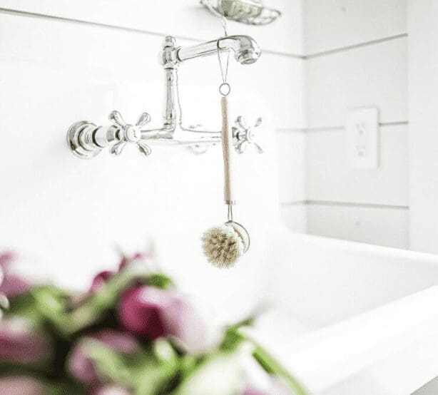 A wooden handled scrub brush hangs on a silver faucet. Image from The Vintage Society Co. a great source for Home Organization supplies