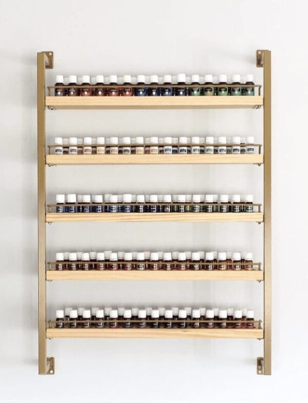 A gold wall rack with wooden shelves holds colorful essential oil bottles